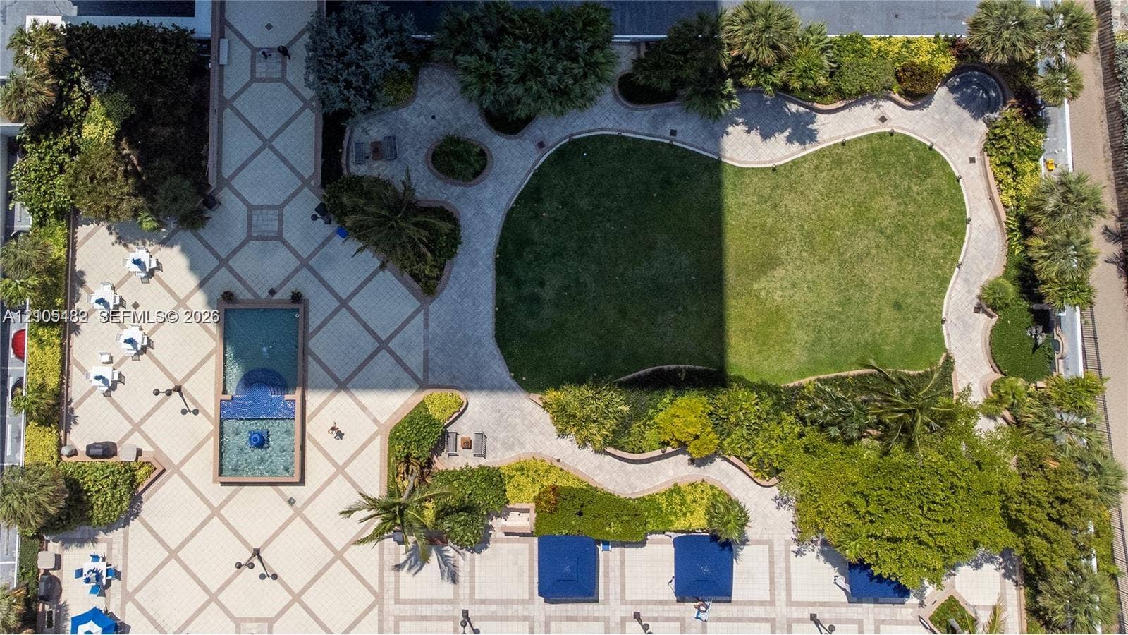 2100 S Ocean Lane, #808, Fort Lauderdale, FL 33316 Aerial view of outdoor grounds featuring a landscaped lawn, stone-paved walkways, a pool with a tile-accented water feature, and established tropical vegetation