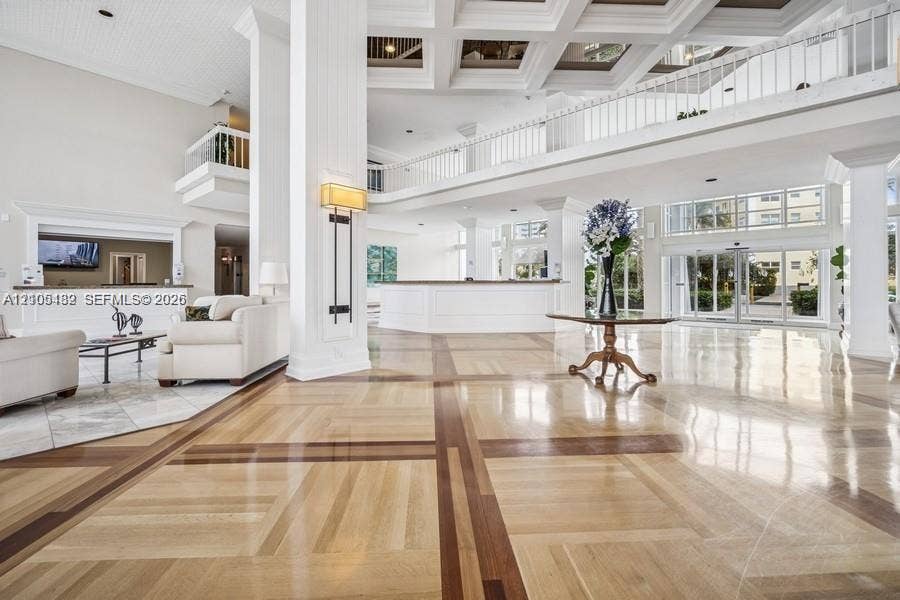 2100 S Ocean Lane, #808, Fort Lauderdale, FL 33316 Grand lobby featuring double-height coffered ceilings, multi-tonal inlay wood-finish flooring, a mezzanine level with white balustrade railings, and expansive glass-paneled entry doors