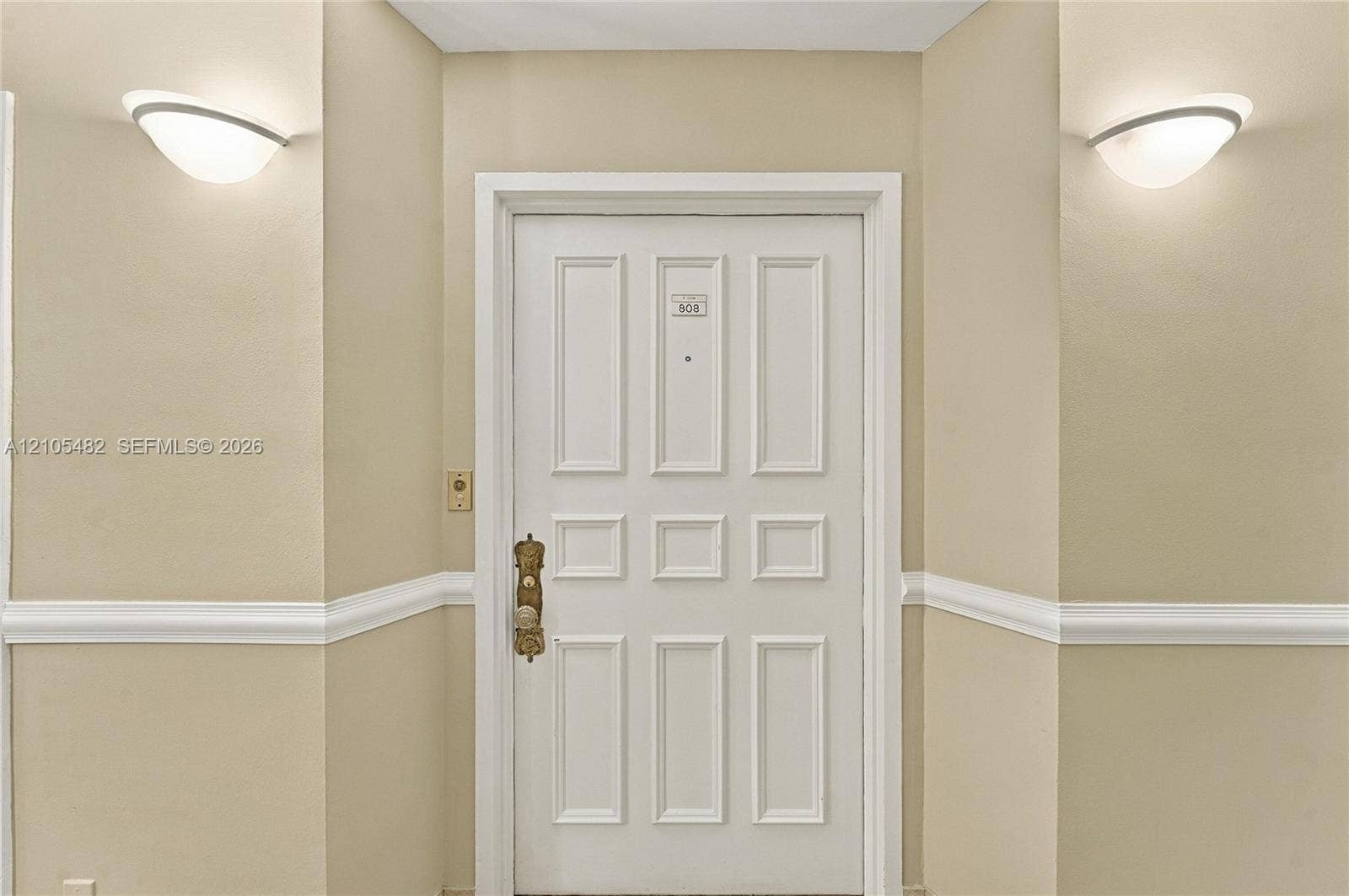 2100 S Ocean Lane, #808, Fort Lauderdale, FL 33316 White six-panel entry door with metallic hardware, dual wall-mounted semi-flush mount fixtures, and chair rail molding