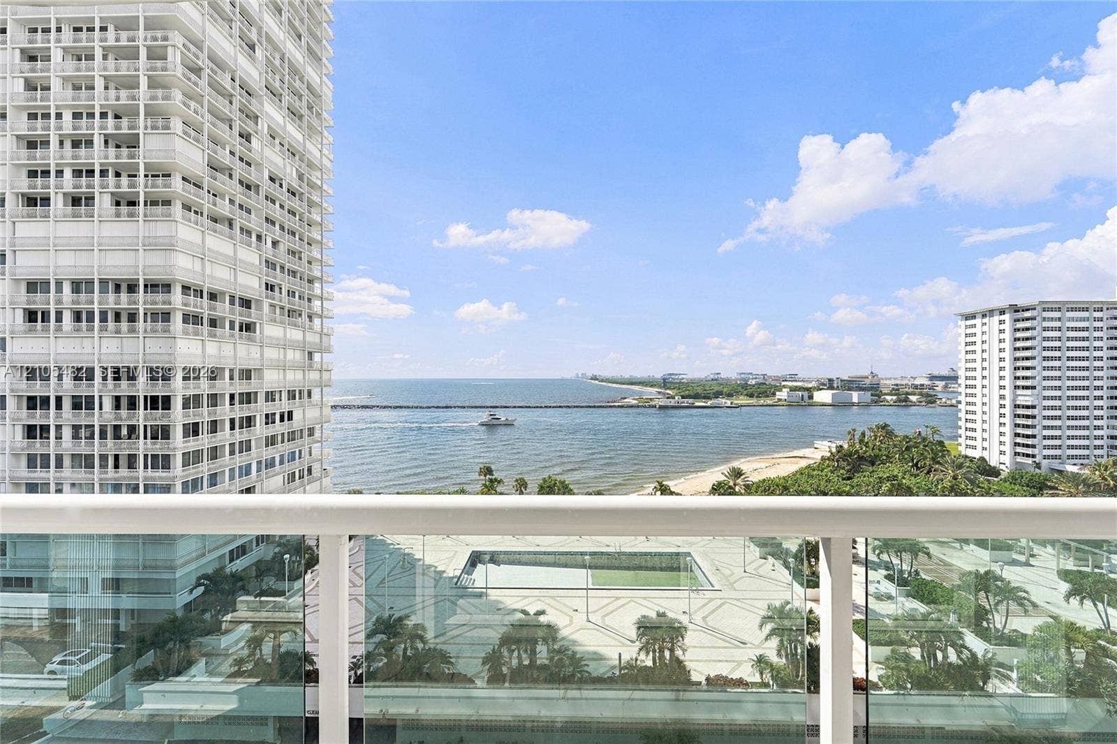2100 S Ocean Lane, #808, Fort Lauderdale, FL 33316 Balcony with a white metal railing and glass paneling, overlooking the ocean and a paved plaza with palm trees