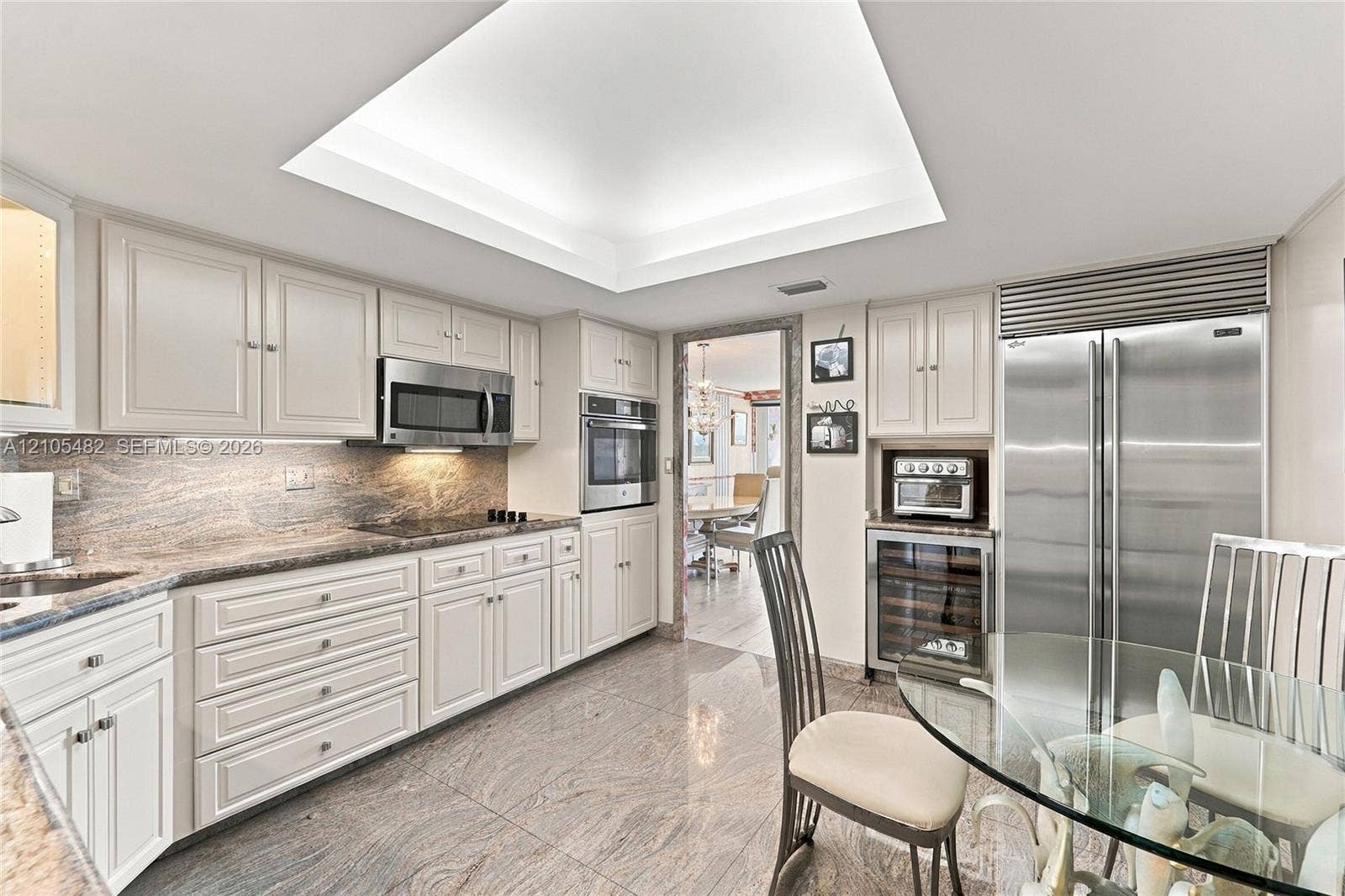 2100 S Ocean Lane, #808, Fort Lauderdale, FL 33316 Kitchen featuring light-toned cabinetry, stone countertops with matching backsplash, stainless steel appliances, a built-in wine cooler, and a recessed tray ceiling