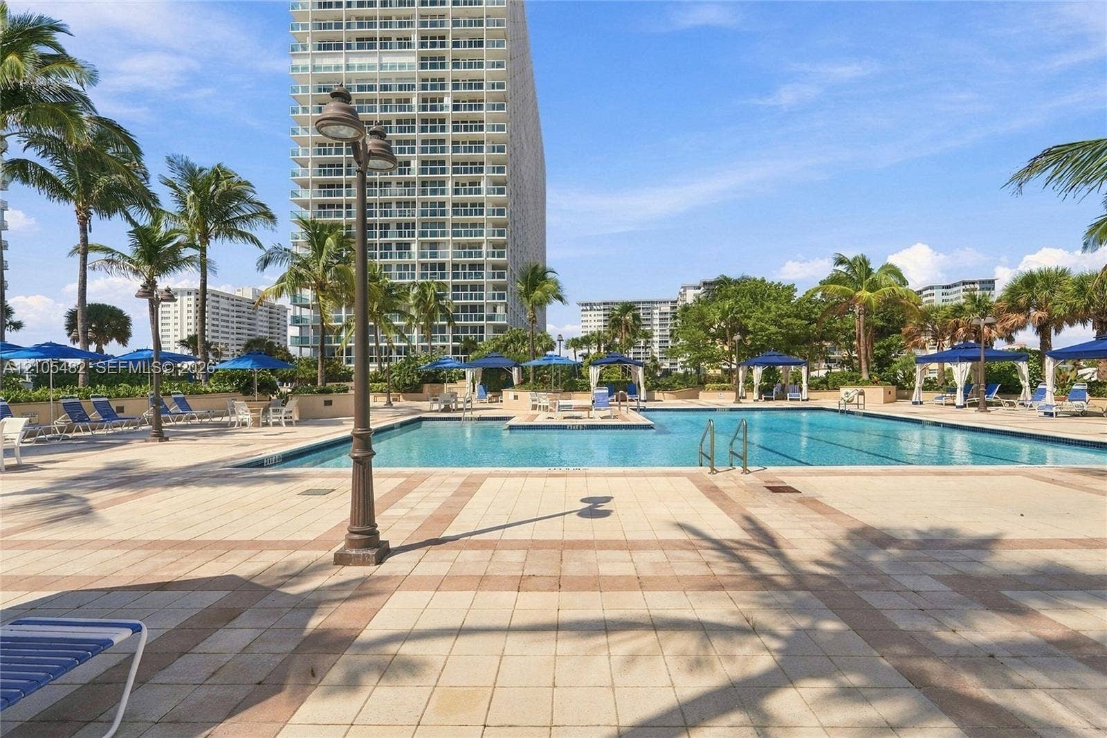 2100 S Ocean Lane, #808, Fort Lauderdale, FL 33316 Swimming pool with tiled decking, poolside cabanas, metal post lamps, and landscaping featuring mature palm trees