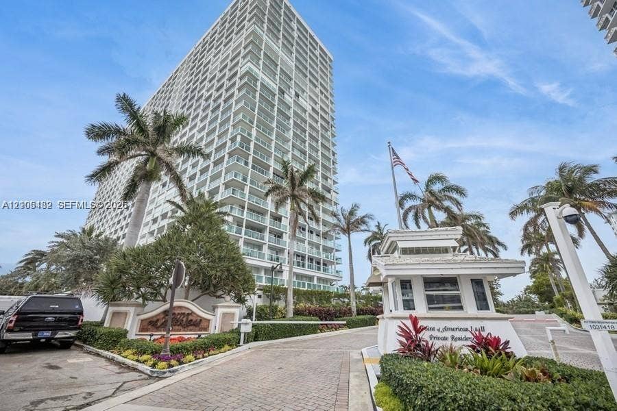 2100 S Ocean Lane, #808, Fort Lauderdale, FL 33316 High-rise residential exterior featuring a gated entry with a dedicated security kiosk, paver driveway, and professional landscaping with mature palm trees