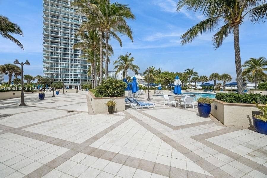 2100 S Ocean Lane, #808, Fort Lauderdale, FL 33316 Pool deck featuring light-toned stone paving, geometric tile patterns, perimeter landscaping with mature palms, and integrated low-profile retaining walls