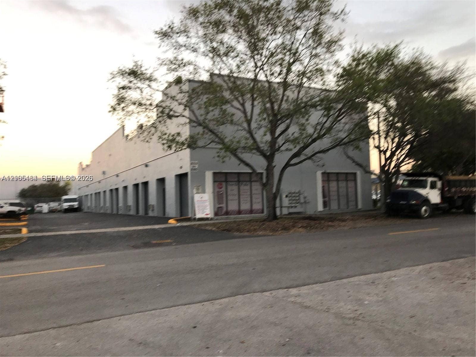 Concrete block construction with multiple roll-up doors, prominent storefront windows, and an asphalt parking area