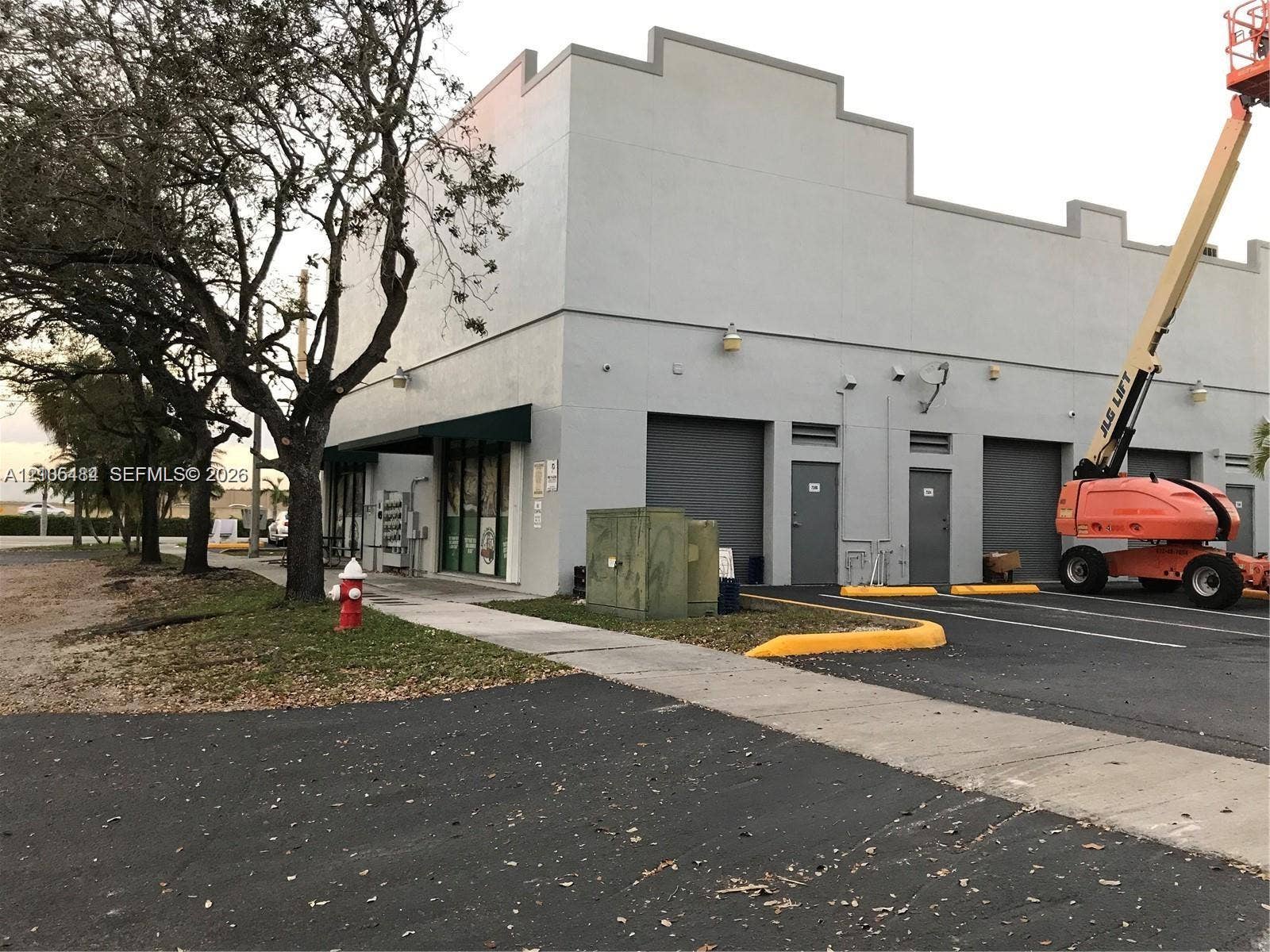 Commercial building exterior featuring a stucco finish, multiple roll-up doors, and a storefront entrance with green awnings