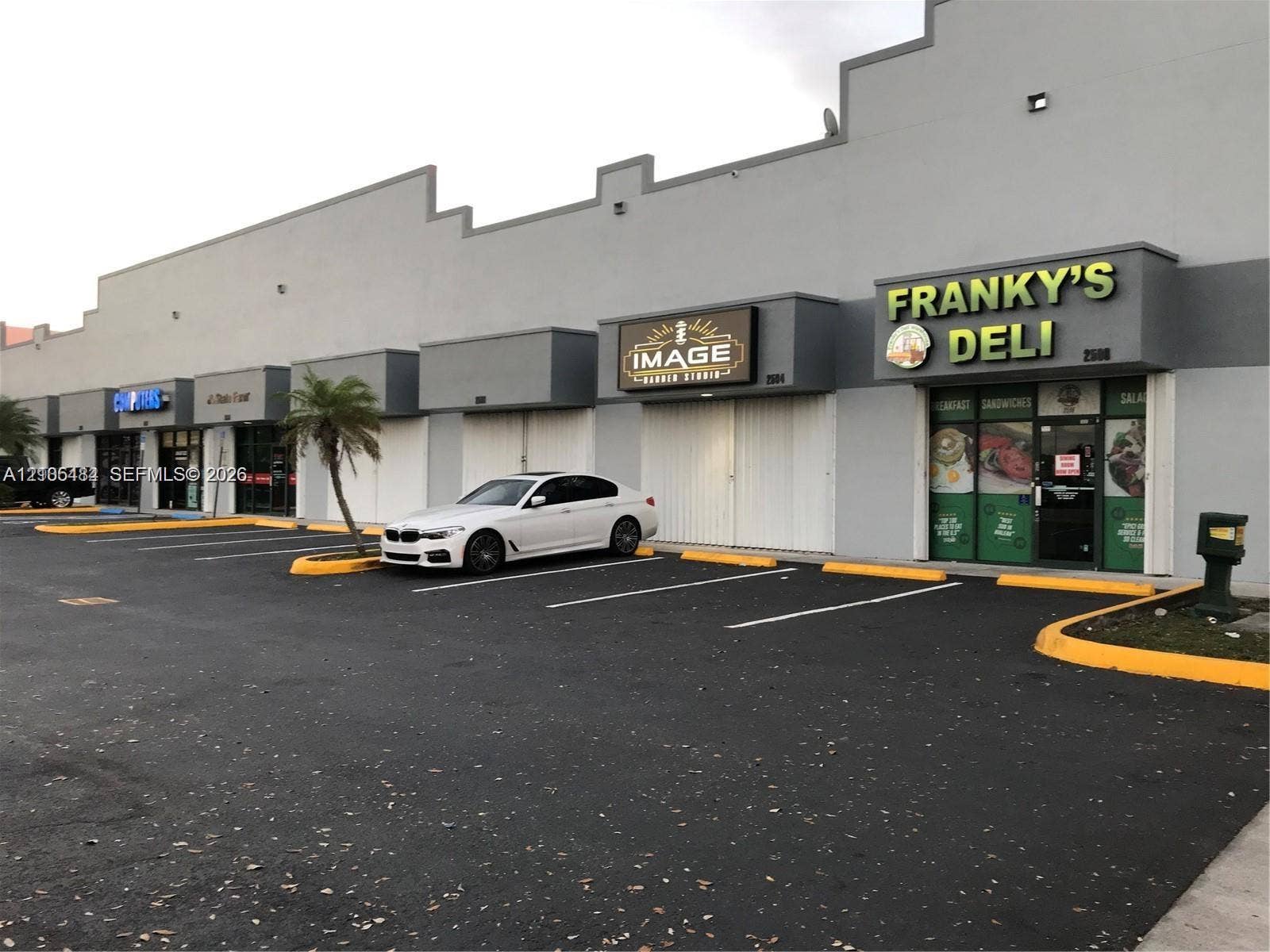 Commercial storefronts with individual signage, ample asphalt parking, and yellow curb accents