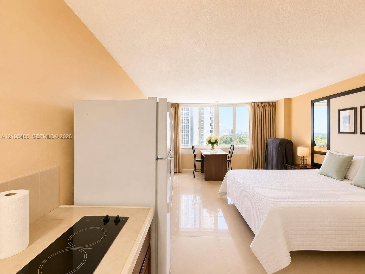 Integrated living space featuring a refrigerator, built-in cooktop, and expansive window with cityscape backdrop