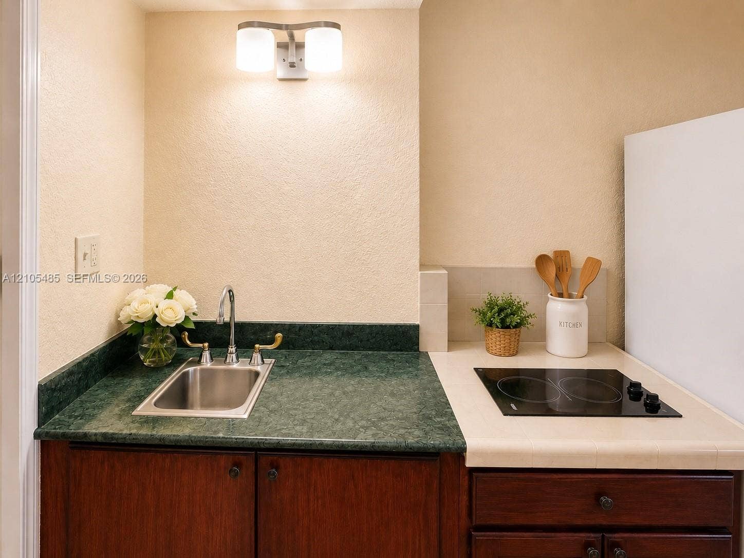 Compact kitchenette featuring a stainless steel sink, dark wood-finish cabinetry, green stone-look countertop, and a built-in electric cooktop