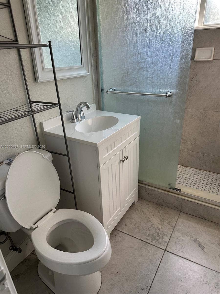Bathroom featuring a white vanity with integrated sink, chrome faucet, tiled flooring, and a glass-enclosed shower with a grab bar