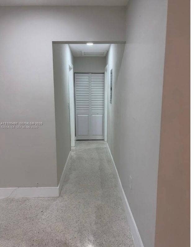 Recessed lighting illuminates a hallway with light-colored walls, white trim, and a textured floor