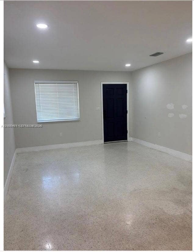 Recessed lighting, light gray wall paint, white window blinds, dark paneled door, and polished aggregate flooring