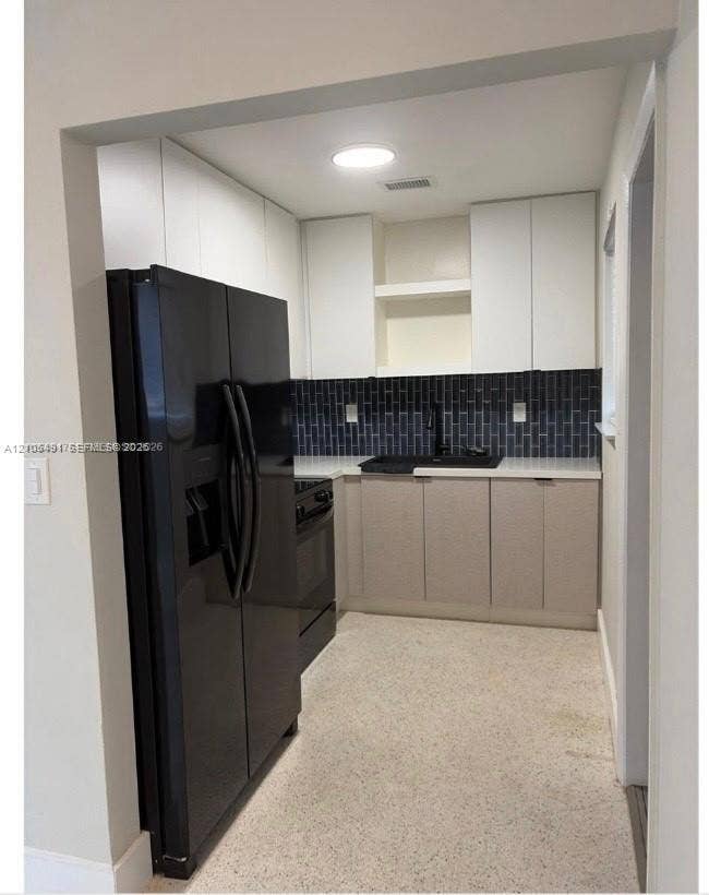 Black subway tile backsplash, white upper cabinetry, light-toned lower cabinetry, light-colored flooring, and built-in black appliances