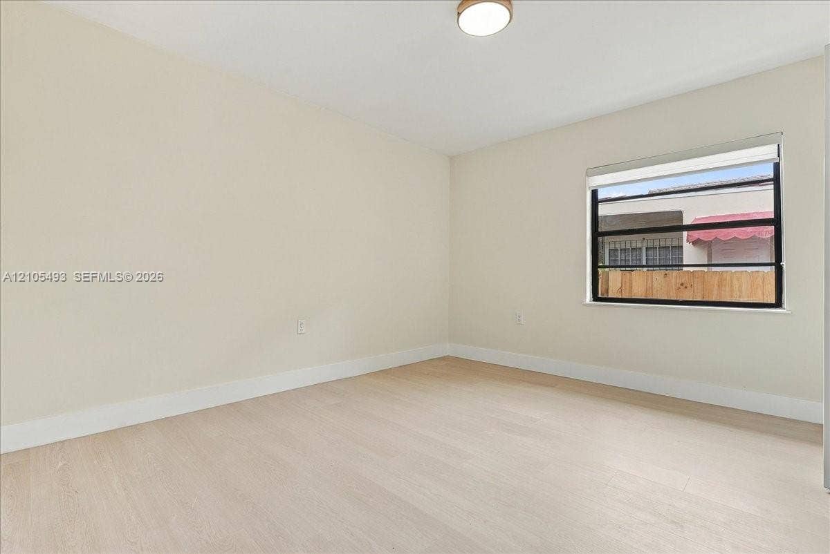 Neutral interior featuring wood-finish flooring, light-toned walls, a single-pane horizontal window with a fitted roller shade, and a flush-mount overhead light fixture