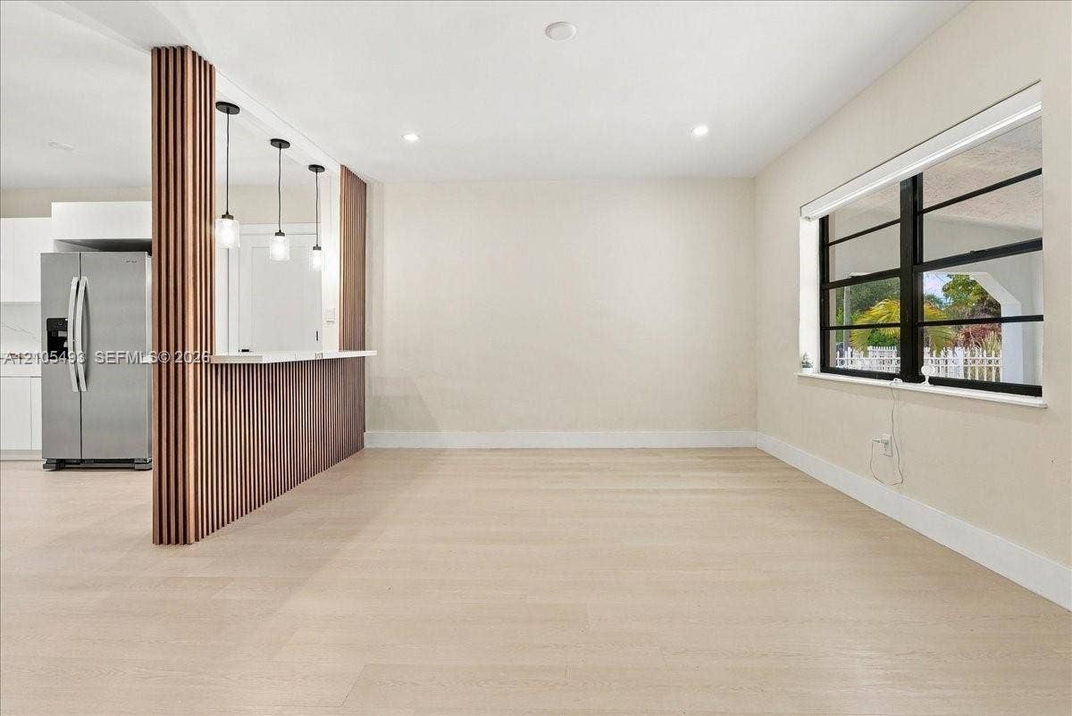 Wood-finish flooring, custom vertical slat wood-finish partition wall, built-in breakfast bar with quartz countertop, pendant lighting, and horizontal multi-pane windows with black framing