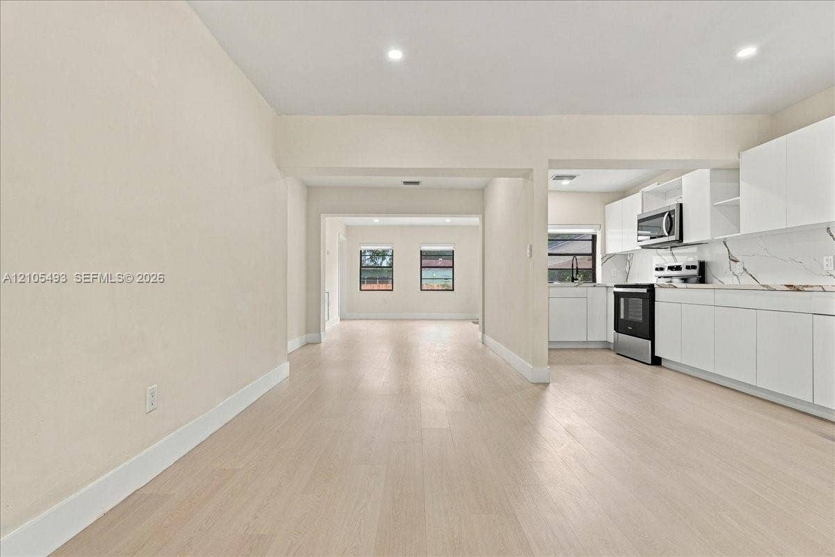 Kitchen featuring white cabinetry, stone-look countertops, stainless steel microwave, and wood-finish flooring throughout