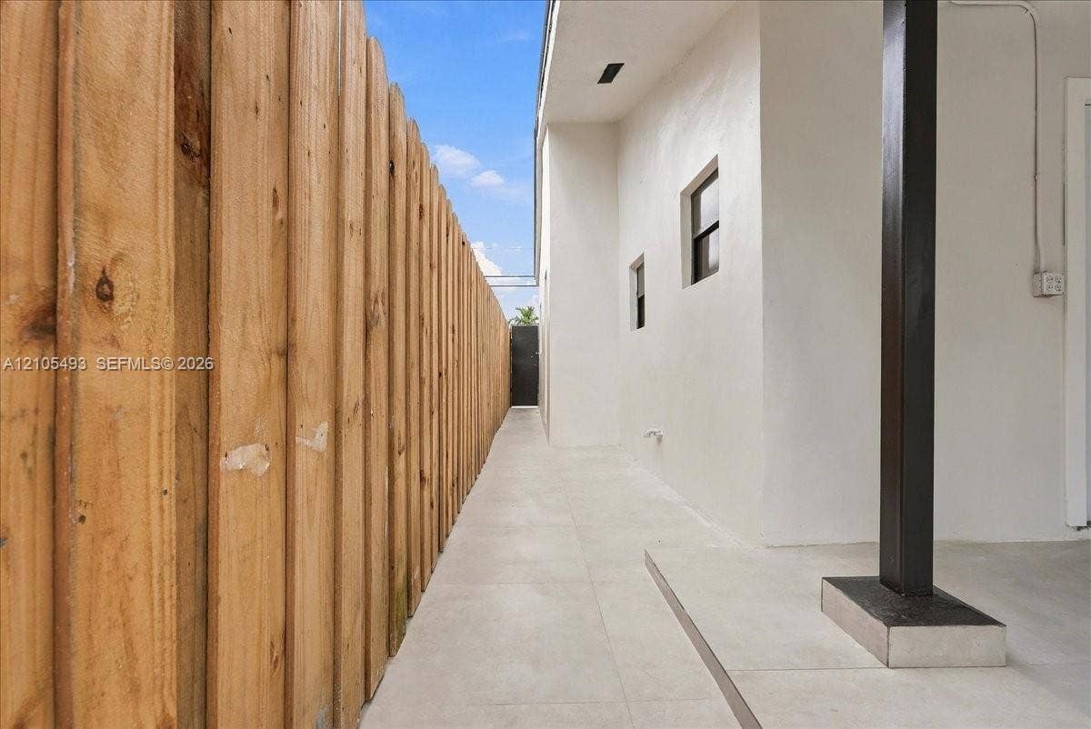Exterior side passage featuring light-toned tile flooring, smooth stucco wall finish, and a full-height vertical wood privacy fence