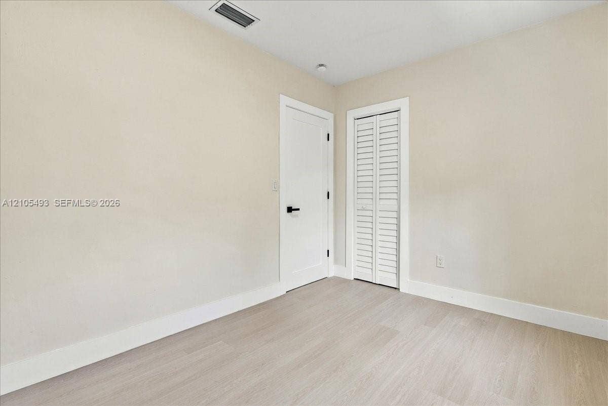 Neutral-toned interior space featuring light wood-finish flooring, a solid-panel door with matte black hardware, and a bifold closet door with louvered panels