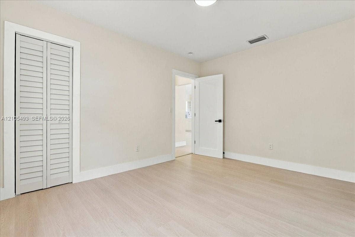 Neutral-toned interior featuring wood-finish flooring, white louvered bi-fold closet doors, and a solid-core interior door with matte black hardware