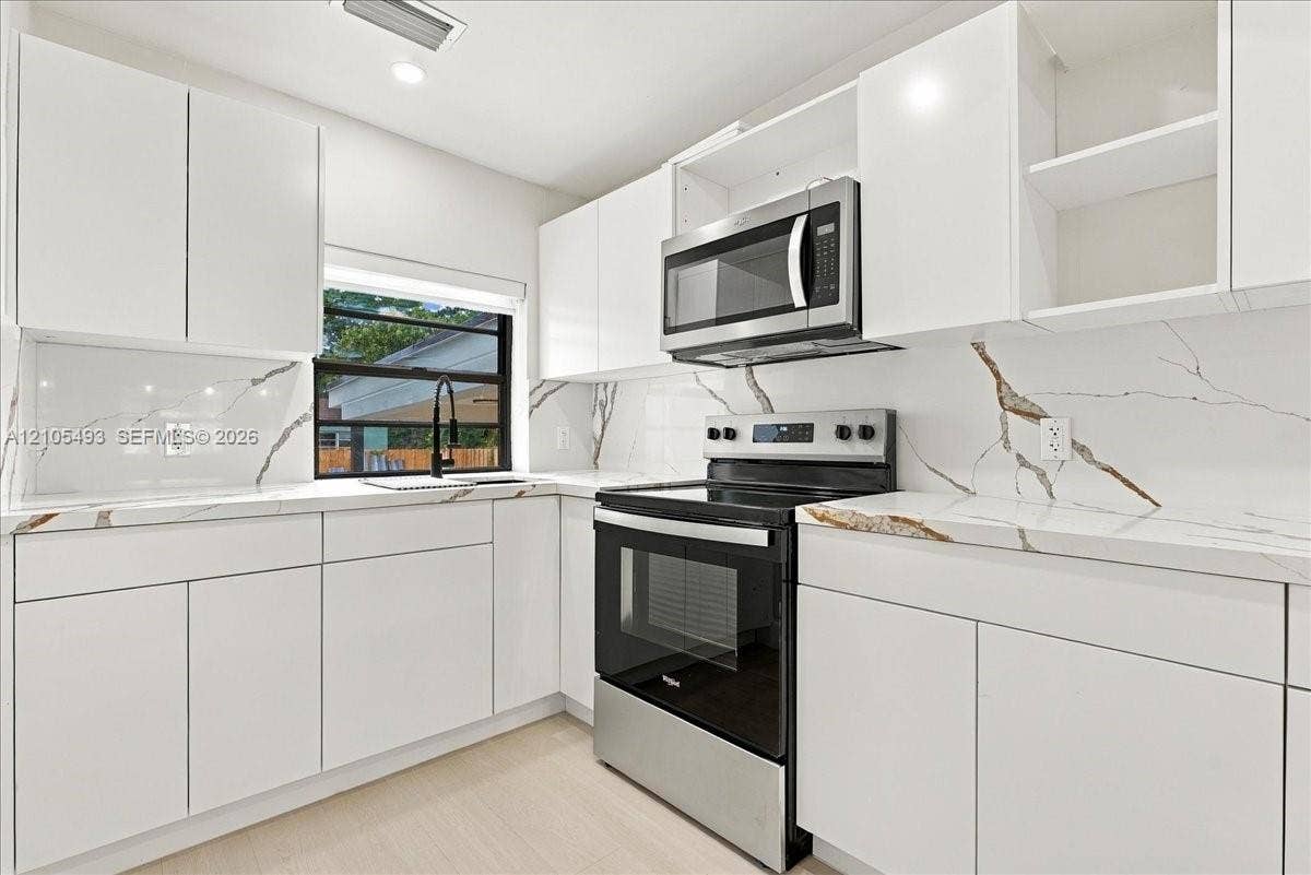 Kitchen featuring white flat-panel cabinetry, stone-patterned countertops, matching full-height backsplash, stainless steel appliances, and a matte black faucet