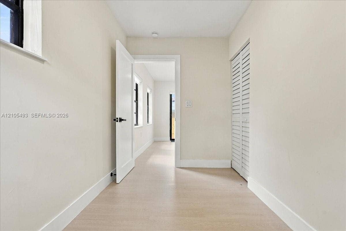 Interior space featuring neutral wall paint, wood-finish flooring, a white paneled door with matte black hardware, and white louvered closet doors