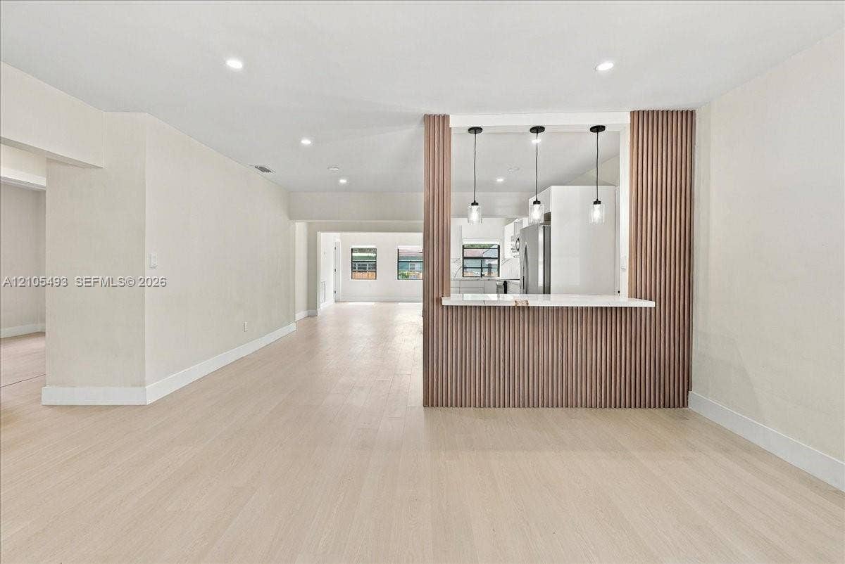 Kitchen pass-through featuring a white stone countertop, vertical wood-slat accent wall, three glass pendant lights, recessed ceiling lighting, and wood-finish flooring