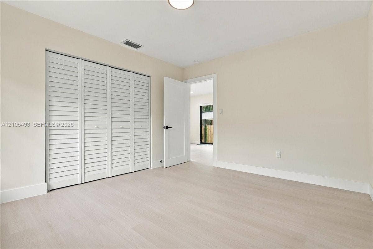 Interior space featuring light wood-finish flooring, neutral wall paint, white bi-fold louvered closet doors, and a shaker-style interior door with matte black hardware