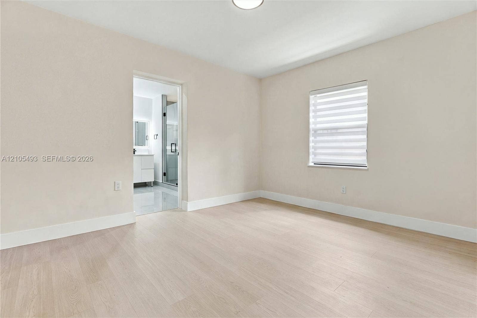 Neutral-toned interior space featuring light wood-finish flooring, a single-window configuration with horizontal blinds, and recessed ceiling lighting