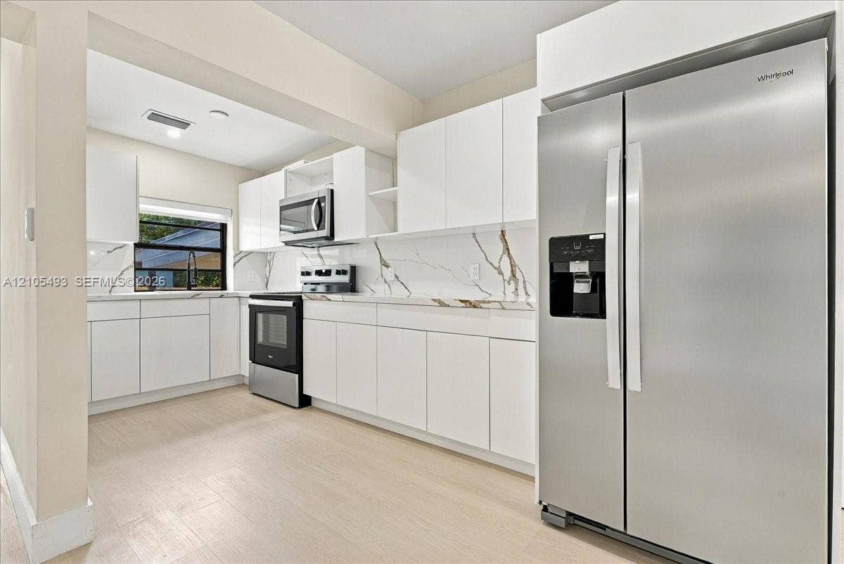 Kitchen featuring white cabinetry, stone-finish countertops with integrated backsplash, stainless steel appliances, and wood-finish flooring
