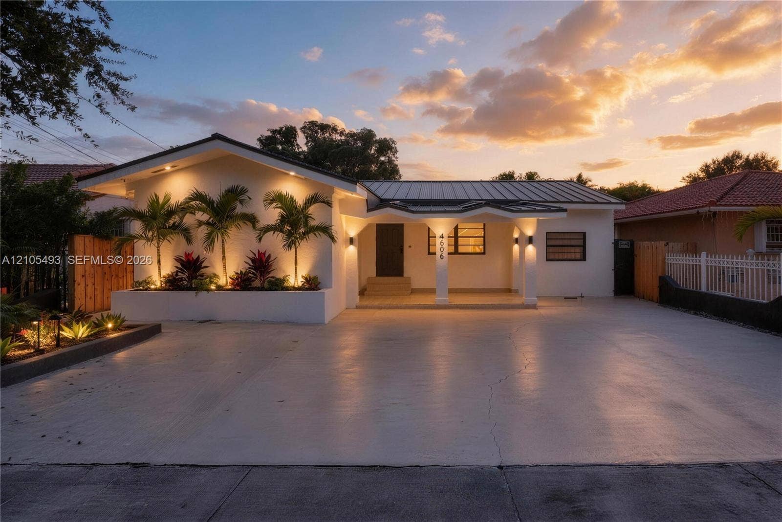 Single-story residence featuring a painted stucco exterior, metal roofing, covered entryway with arched support pillars, and integrated exterior landscape lighting