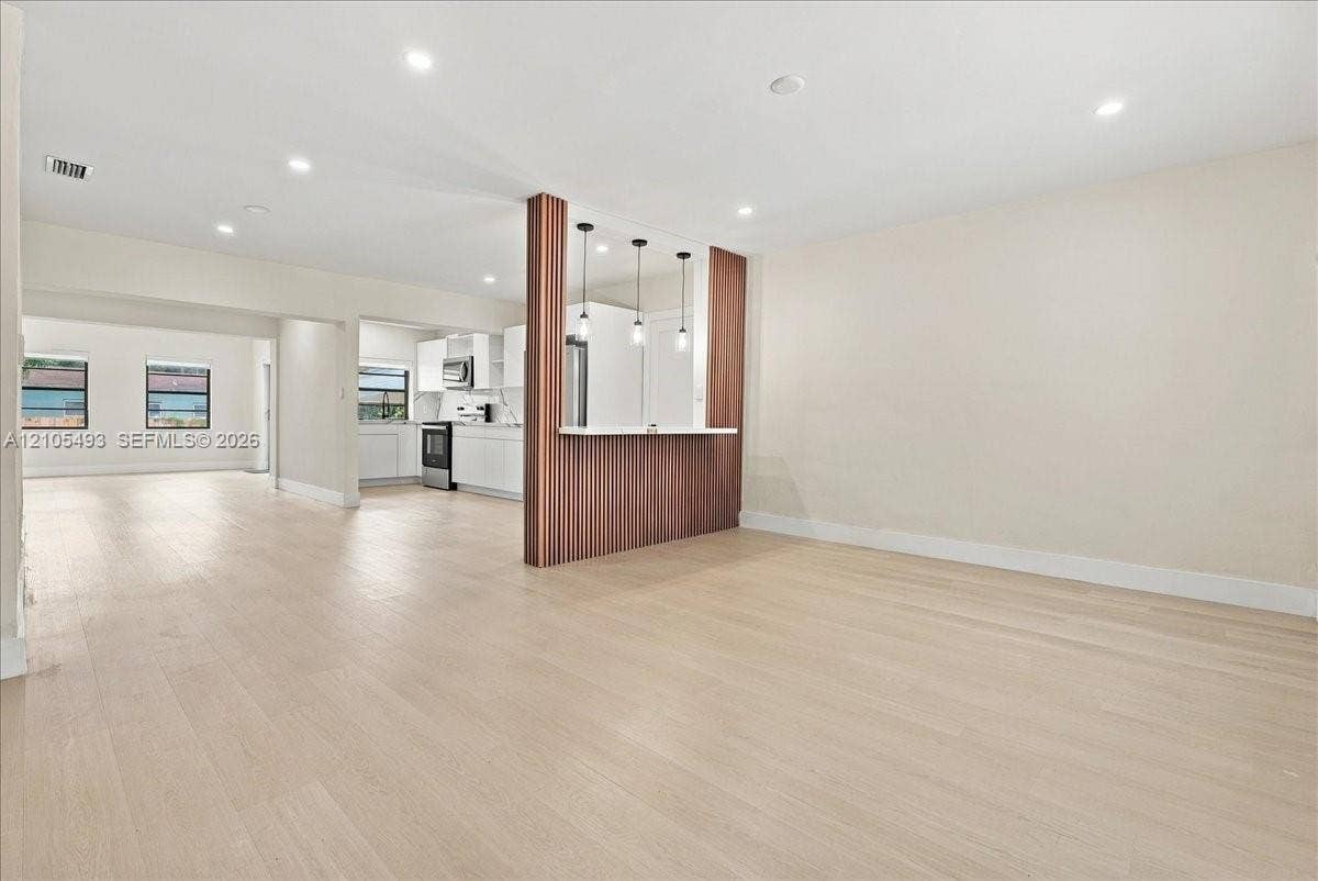 Open floor plan featuring wood-finish flooring, a wood-paneled peninsula with integrated counter seating, recessed lighting, and three pendant lights