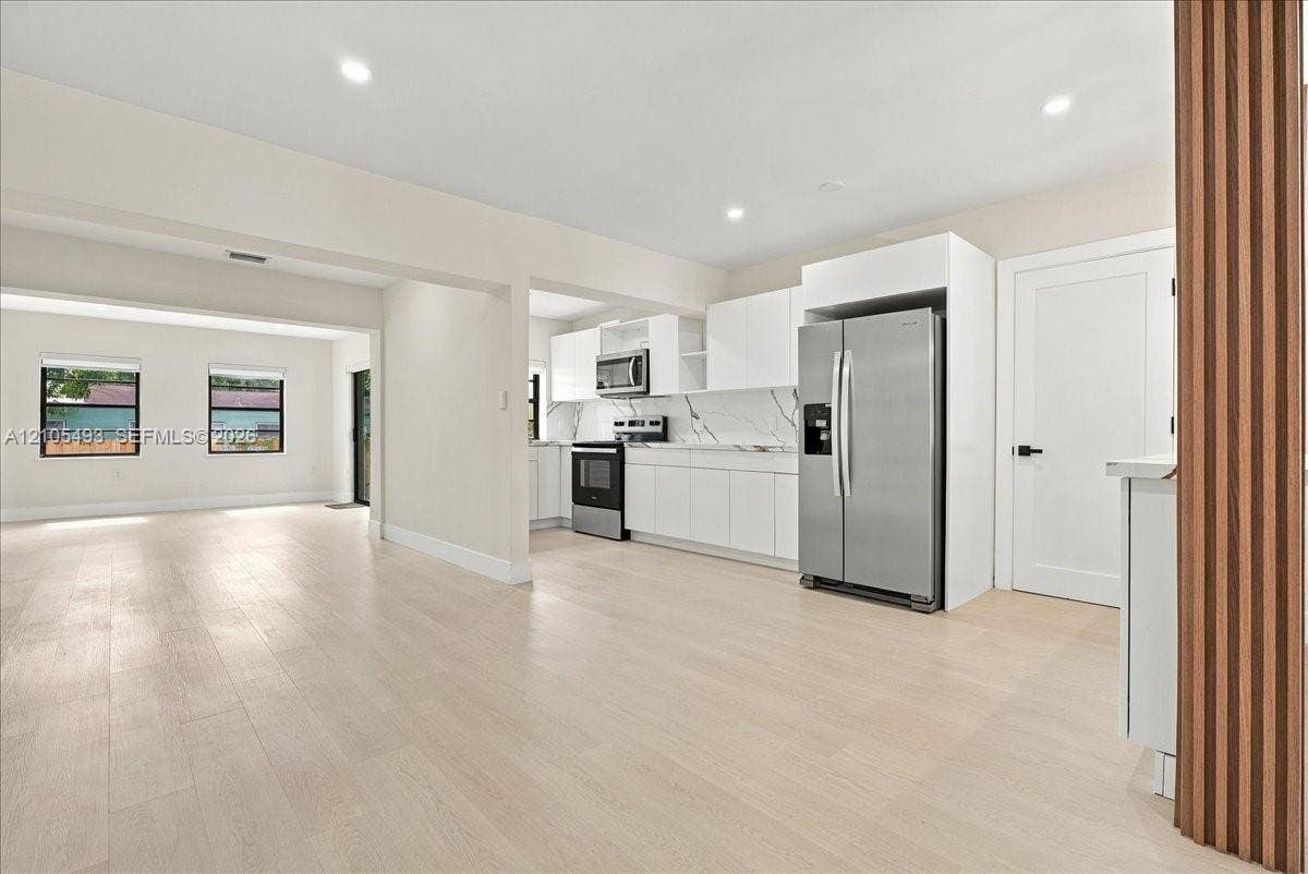 Kitchen featuring white flat-panel cabinetry, stone-patterned backsplash, stainless steel appliances, and wood-finish flooring