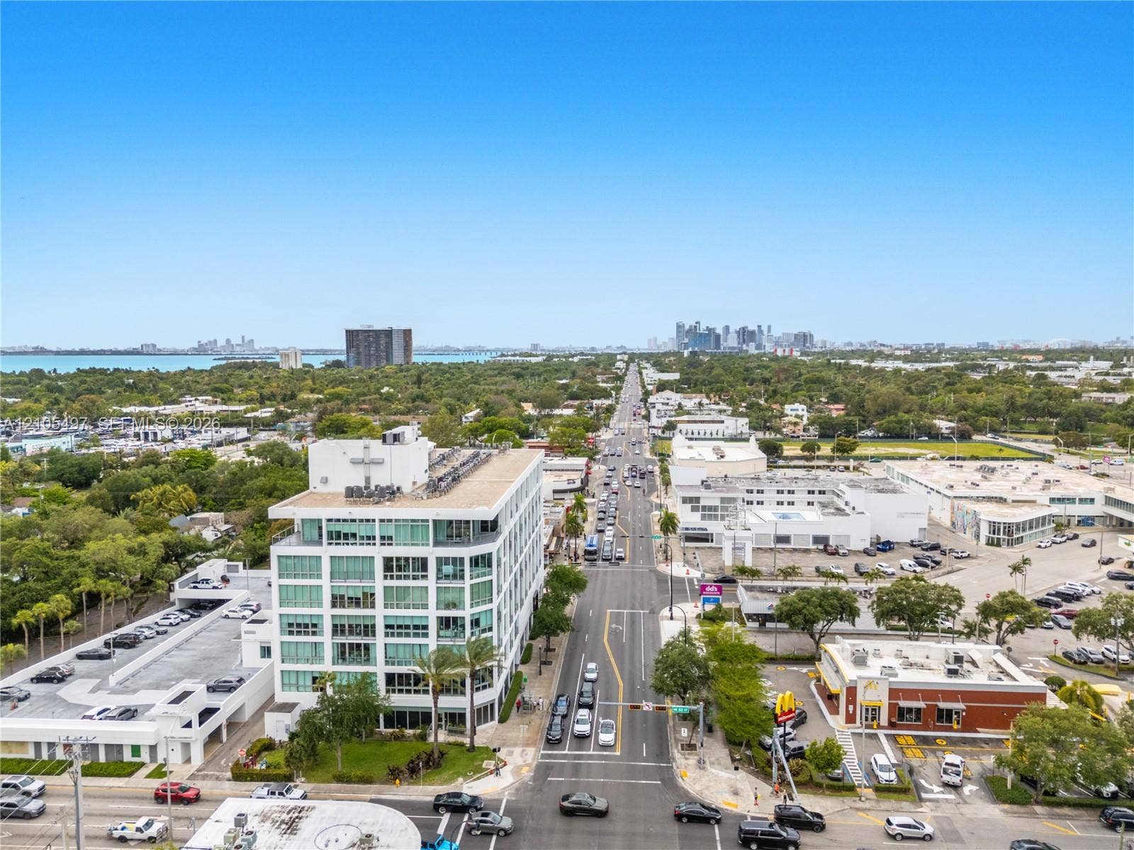 Aerial perspective showcasing a structured streetscape with a prominent multi-story building, an expansive parking structure, and distant water scenery