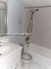 White vanity with integrated sink, white bathtub with shower fixture, and a toilet