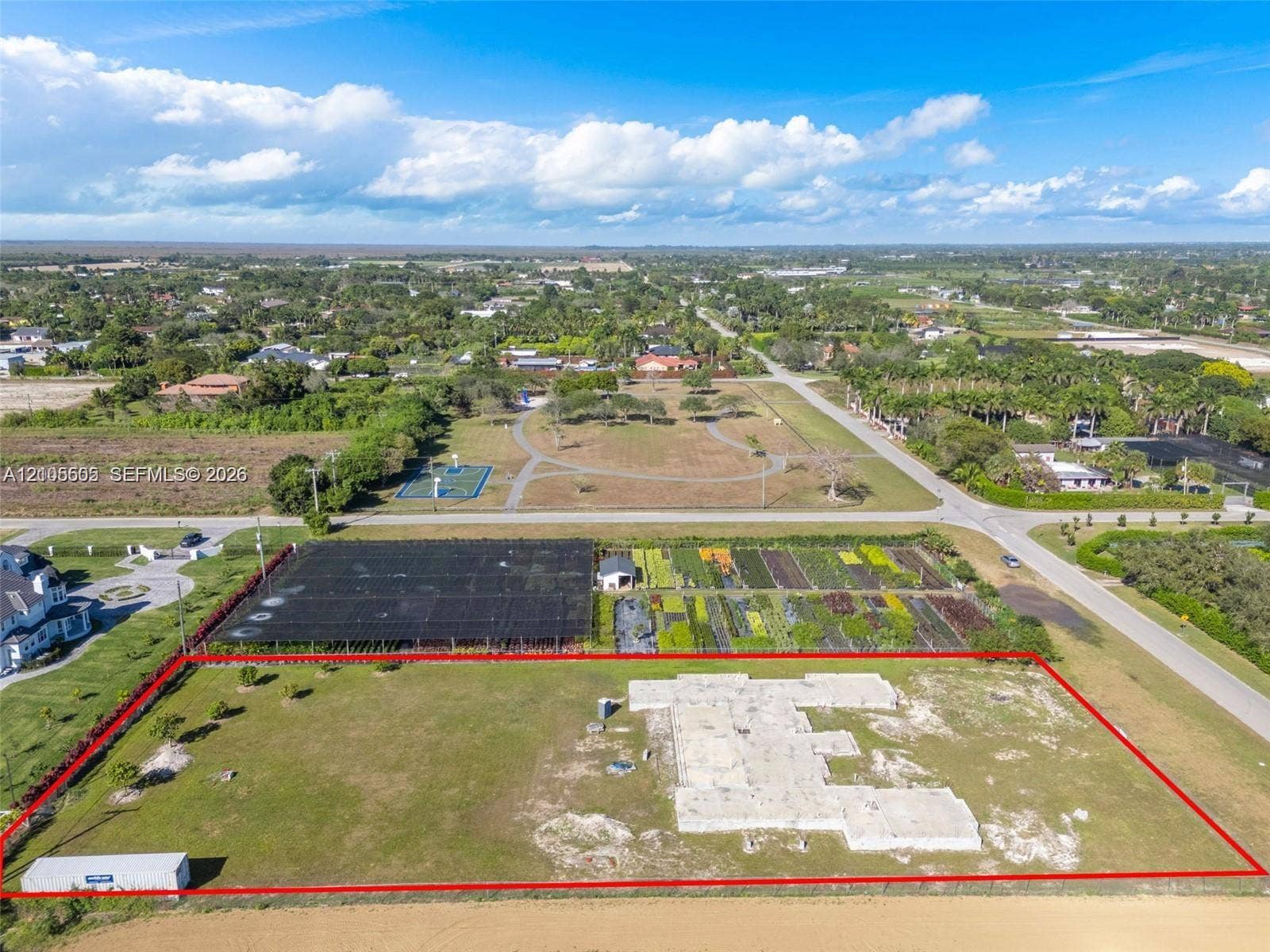 Expansive lot featuring a partial concrete foundation, established cultivation beds, a separate storage structure, and a perimeter fence
