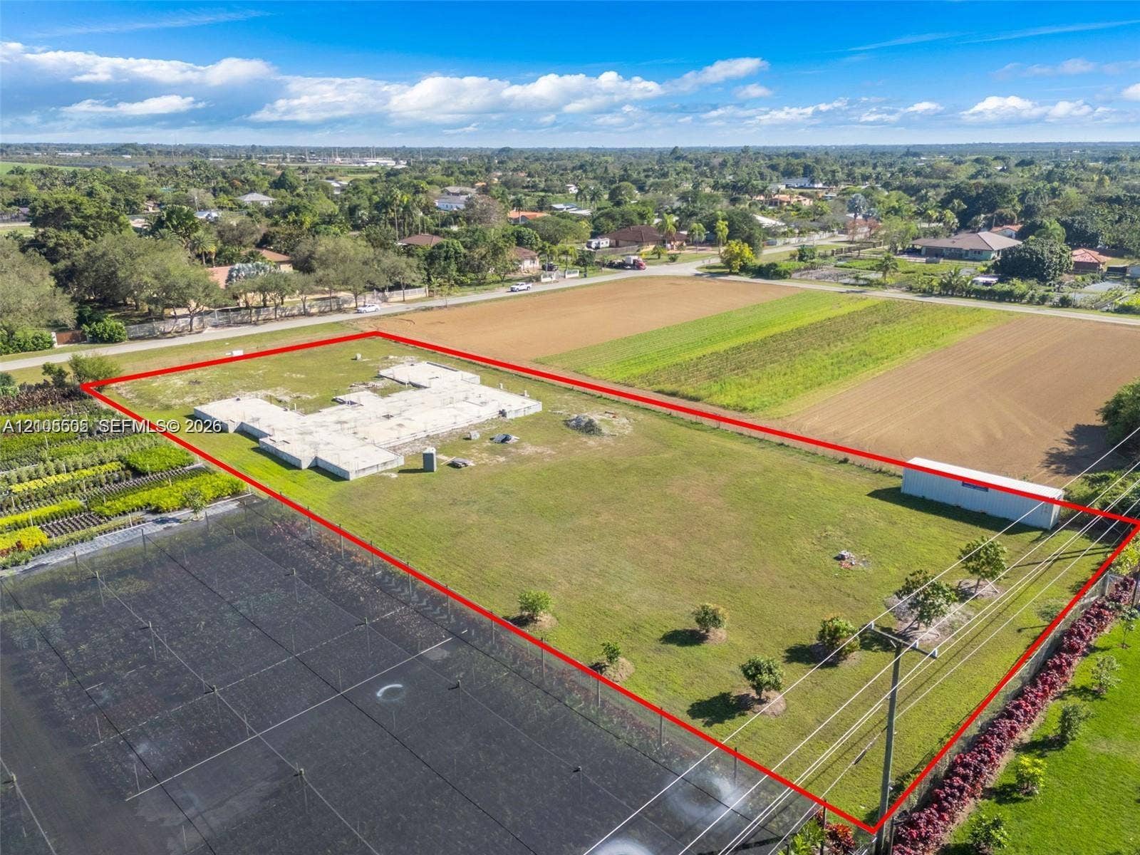 Expansive lot featuring a partial foundation, agricultural fields, and a white storage structure with a red roof