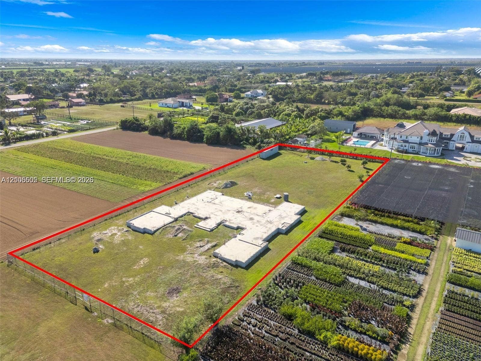 Expansive lot featuring a partial foundation, surrounding green space, and perimeter fencing