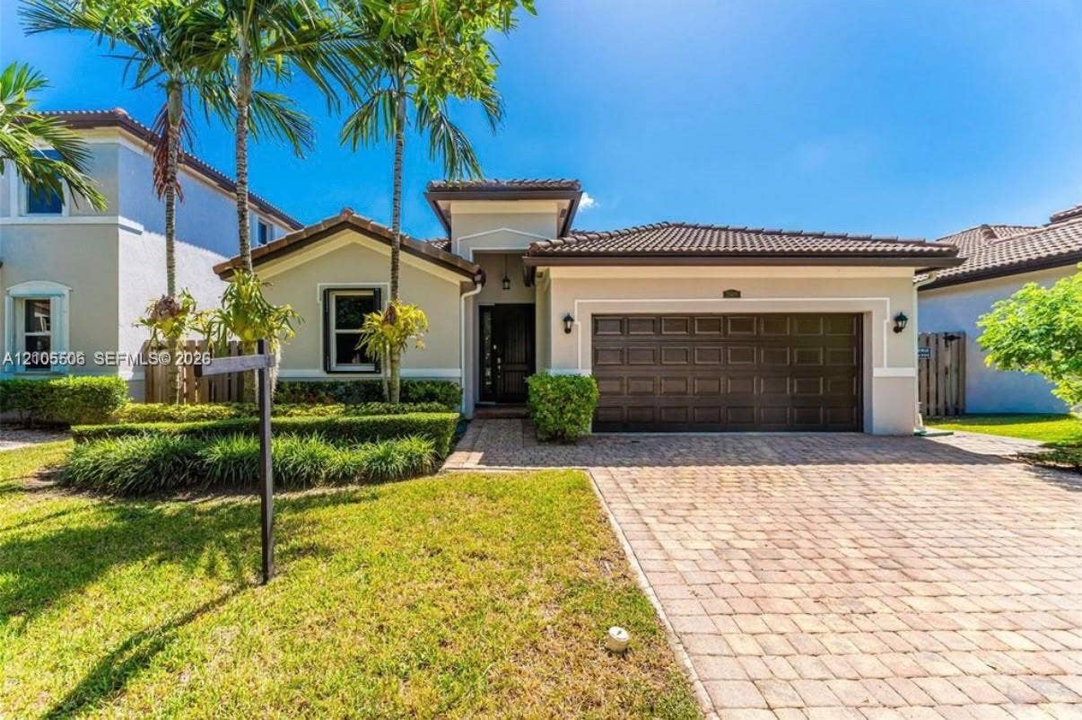 Stucco exterior with a tiled roof, paver driveway, integrated garage, and manicured landscaping