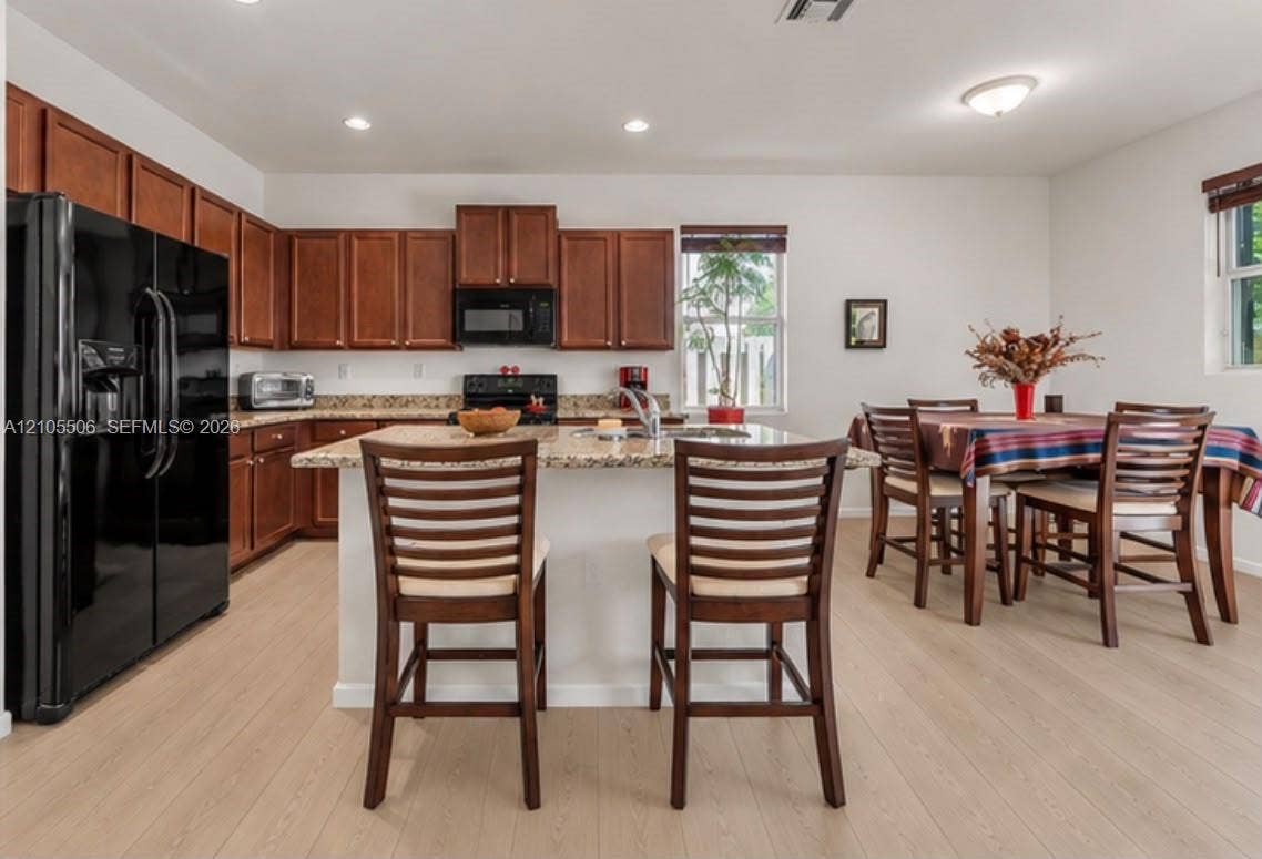 Kitchen featuring wood-finish flooring, granite countertops, wood cabinetry, and a kitchen island with seating