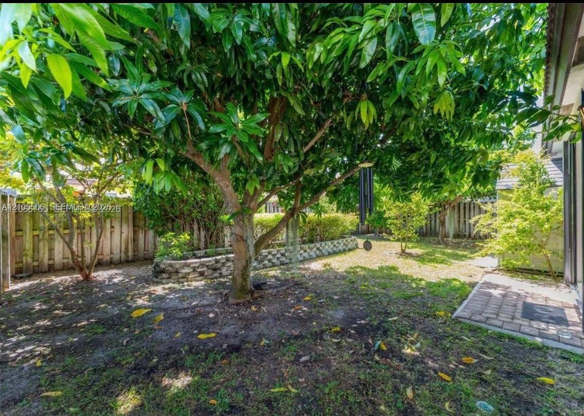 Expansive backyard featuring a mature tree, natural ground cover, a paver patio area, and a wood privacy fence