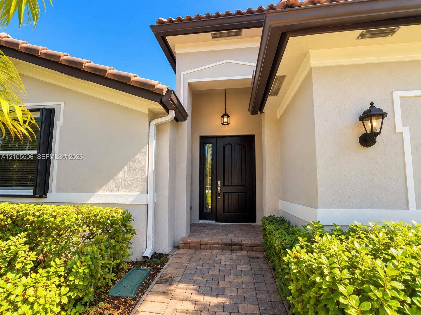 Entryway featuring a dark wood double door, brick paver walkway, and exterior wall sconce