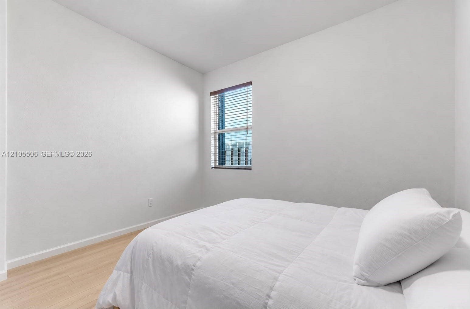 Light-toned wood-finish flooring, white painted walls, and a window with blinds