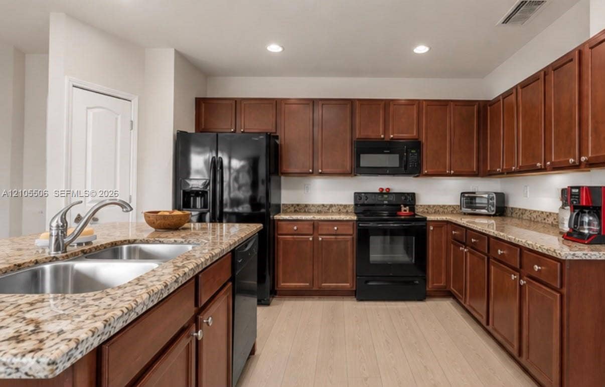 Kitchen featuring wood-finish cabinetry, light-toned countertops, stainless steel double basin sink, and black appliances