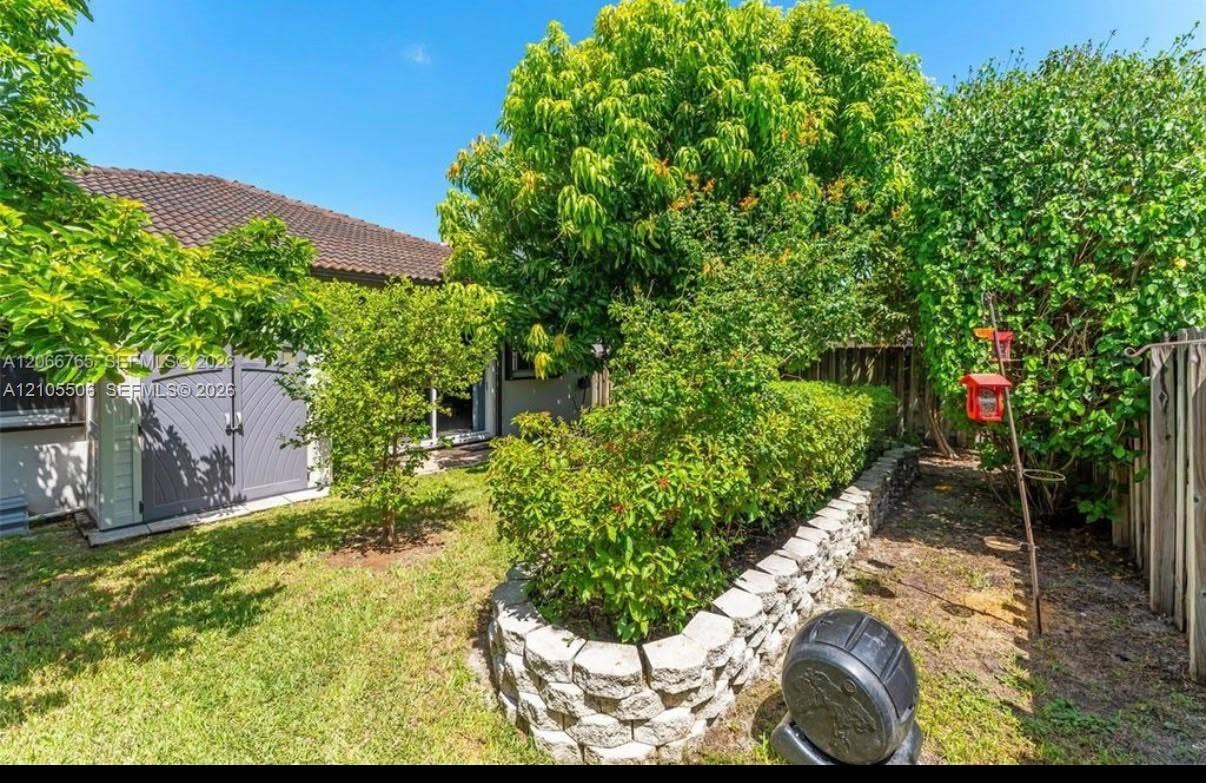 Expansive backyard featuring a manicured lawn, established landscaping, and a concrete paver retaining wall