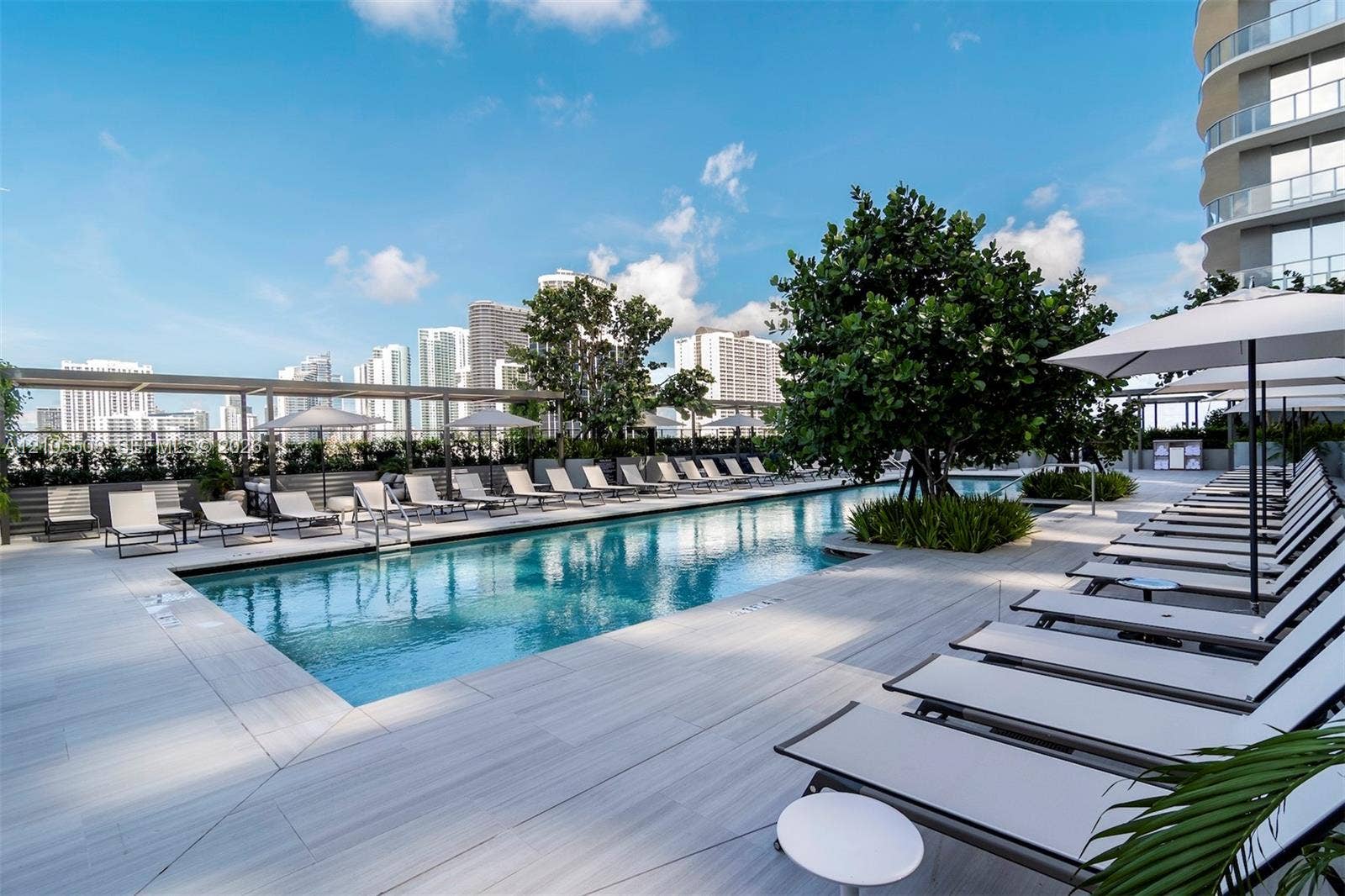 Outdoor swimming pool with surrounding lounge area, paver decking, and mature landscaping