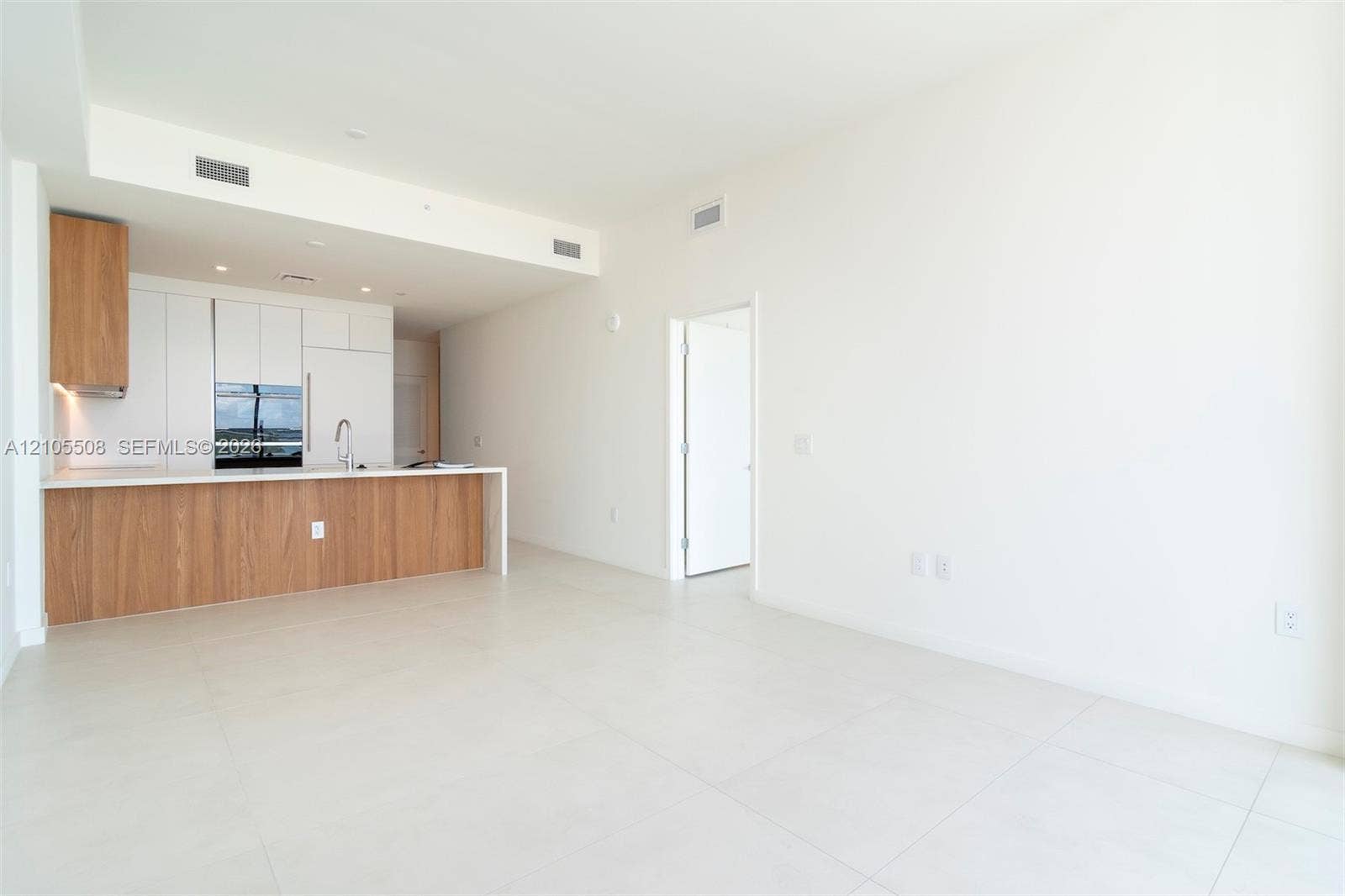Open-concept living space featuring high ceilings, light tile flooring, built-in kitchen cabinetry with integrated appliances, and a kitchen island with a light-toned countertop
