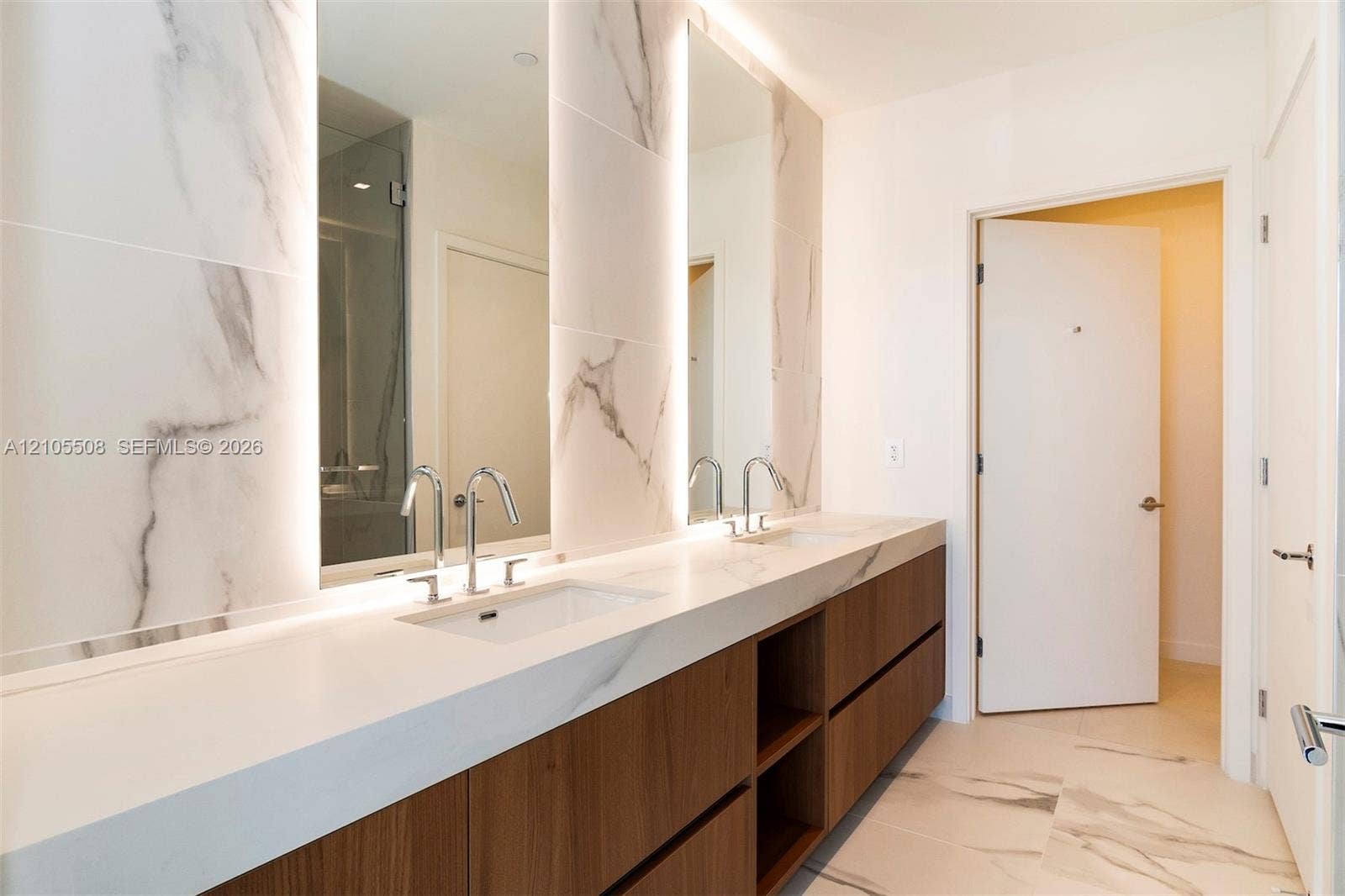 Dual vanity with integrated sinks, wood-finish cabinetry, polished chrome fixtures, and a large wall mirror