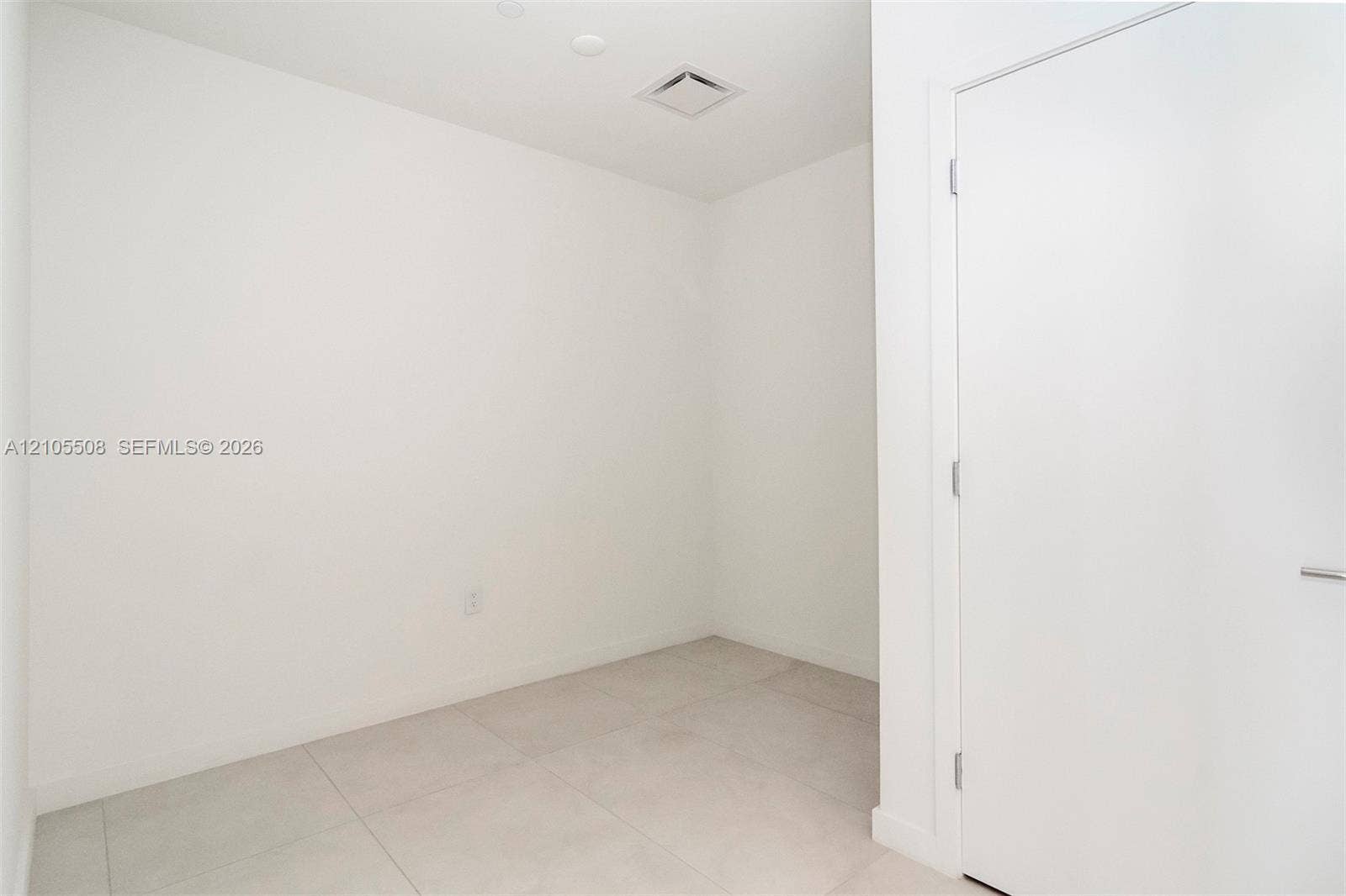 White ceramic tile flooring, recessed ceiling lighting, and a flush-mounted door with a modern handle