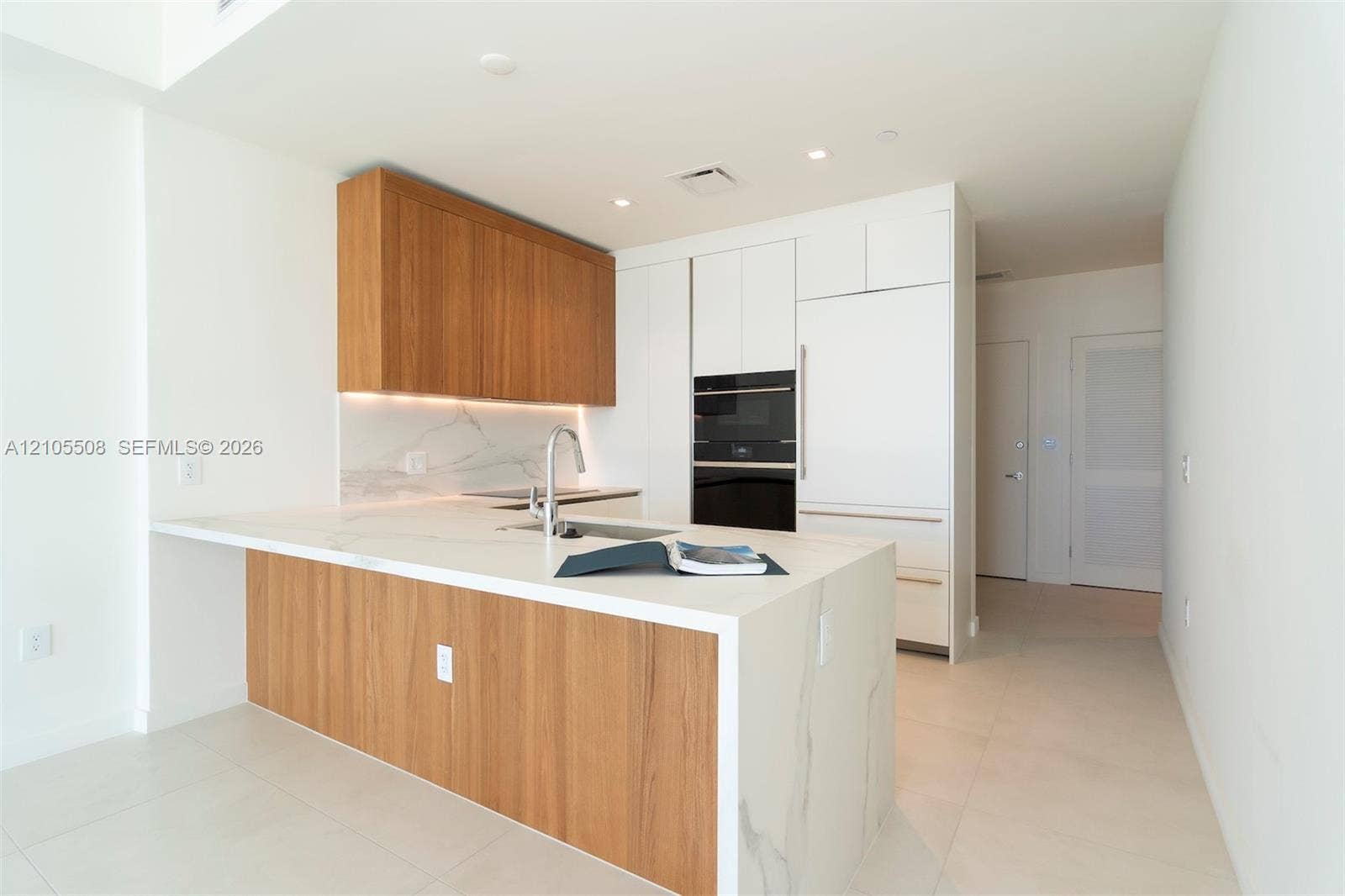 Modern kitchen featuring a waterfall island with wood-finish paneling, under-cabinet lighting, integrated appliances, and a marble-finish backsplash