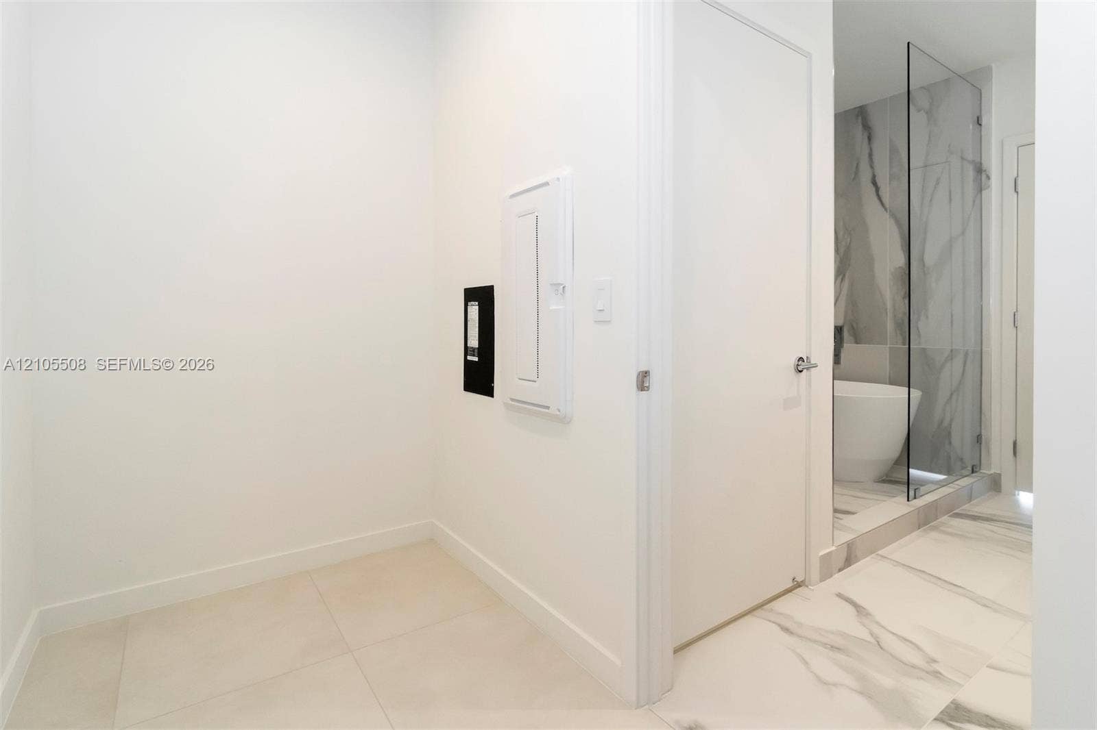 White interior walls, light-toned tile flooring, and a glass-enclosed shower with a marble-patterned tile surround